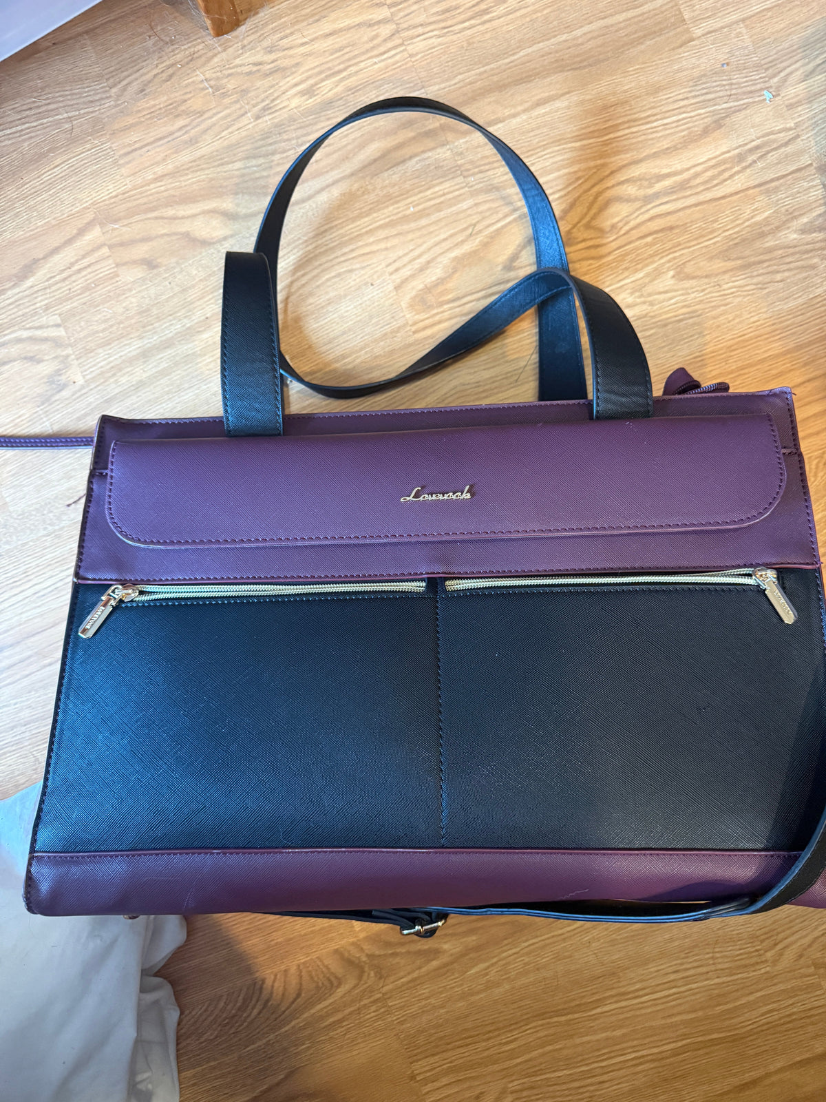 A purple and navy blue leather briefcase or laptop bag with a gold-tone 'Lamark' logo, shown from a top-down view on a wooden floor.